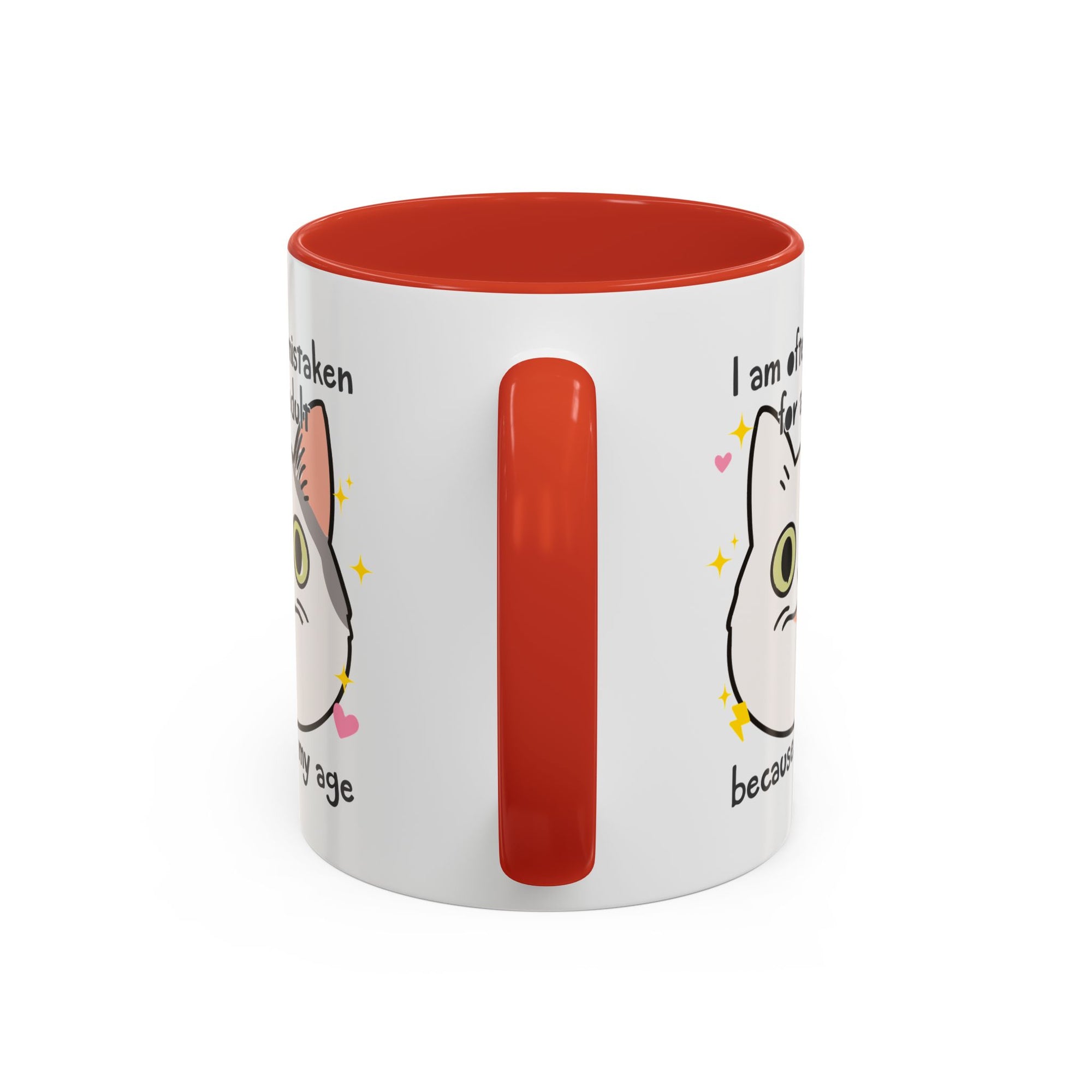 White ceramic mug with red handle and interior featuring a cute wide-eyed cat face, hearts, sparkles, and the phrase “I am often mistaken for an adult because of my age.”
