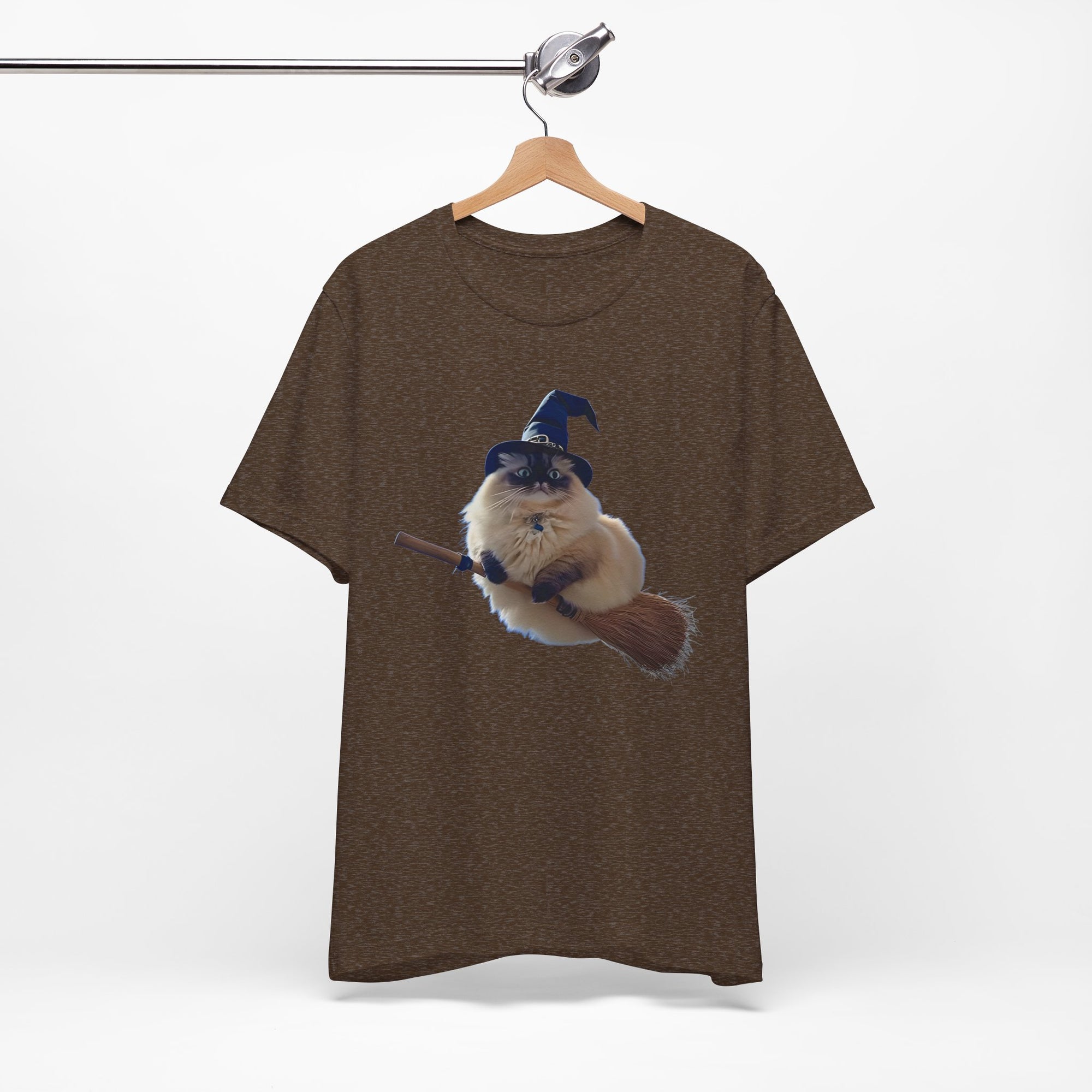 Brown t-shirt with a graphic of a cat in a witch hat on a broomstick, hanging on a wooden hanger against a white background.