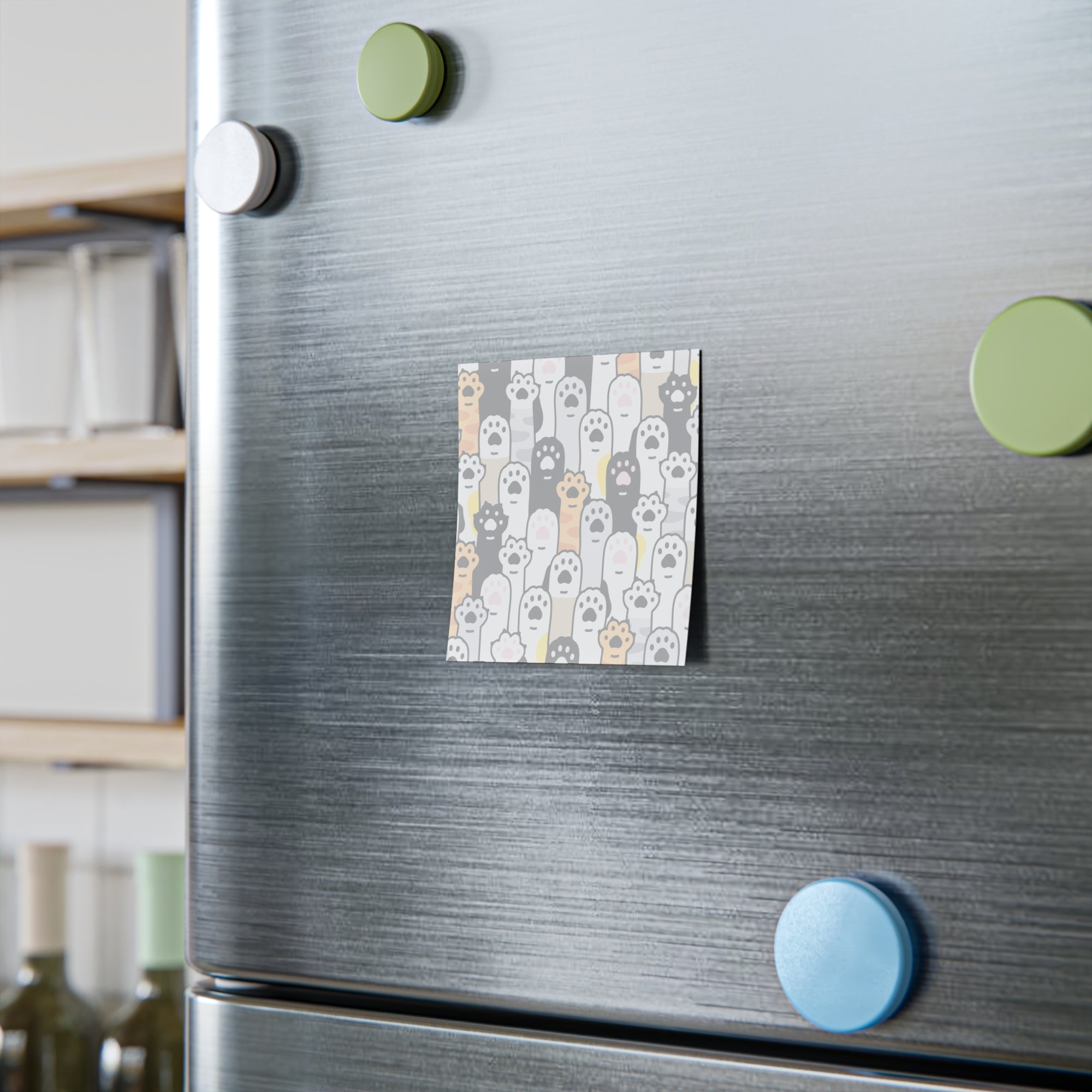 Fridge with a decorative magnet featuring cat illustrations and green and blue magnets on a kitchen background.