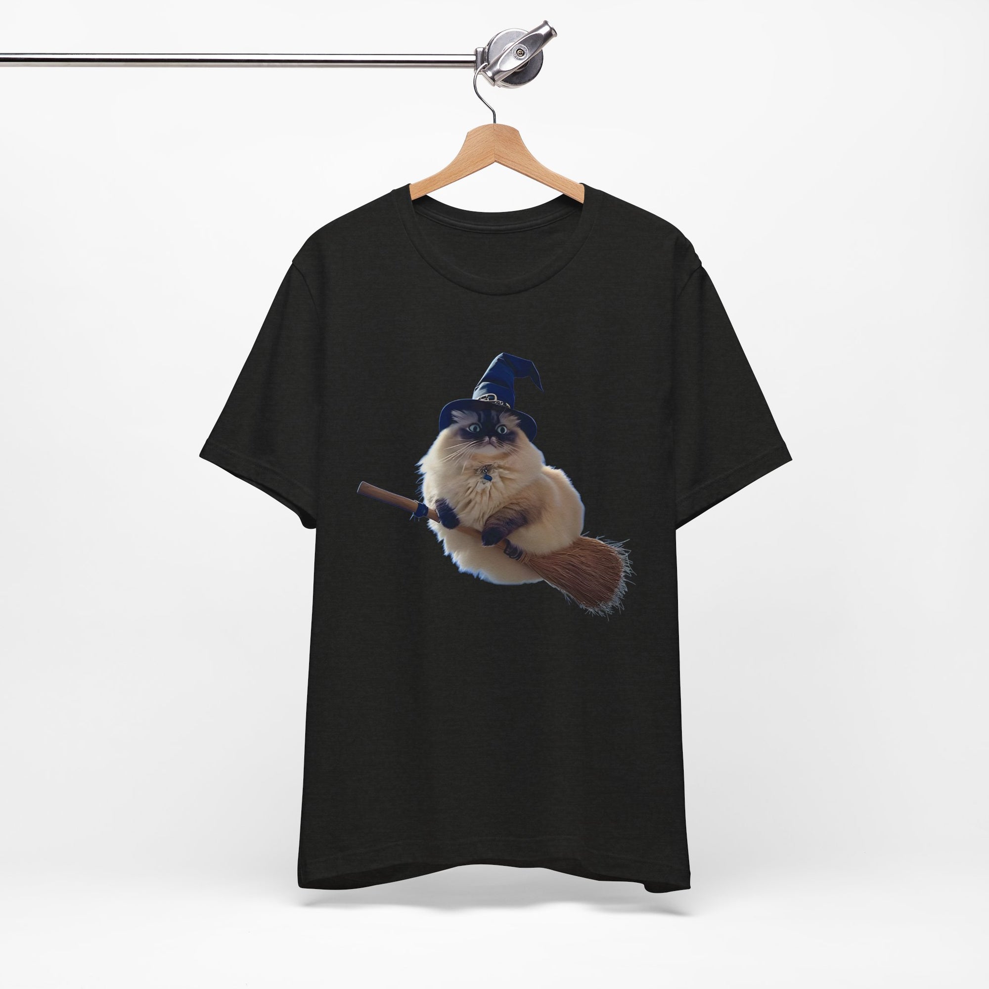 Black t-shirt with a graphic of a cat wearing a witch hat and holding a broomstick, hanging on a wooden hanger against a white background.