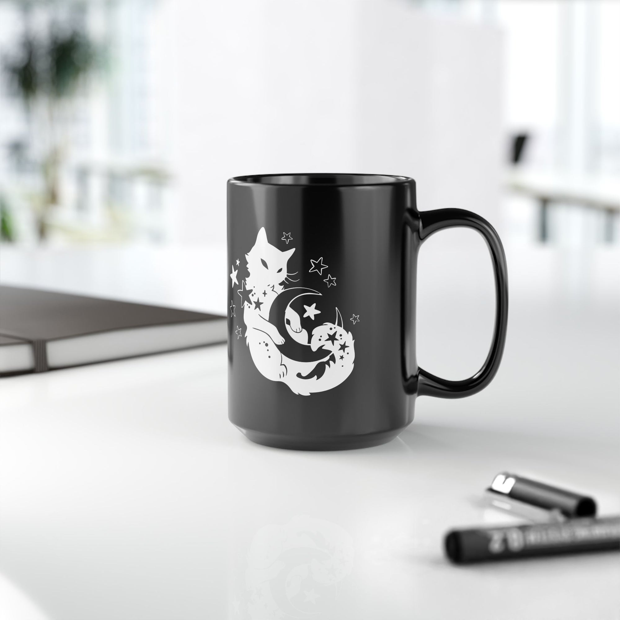 Black mug with a cat on a white surface with office items.