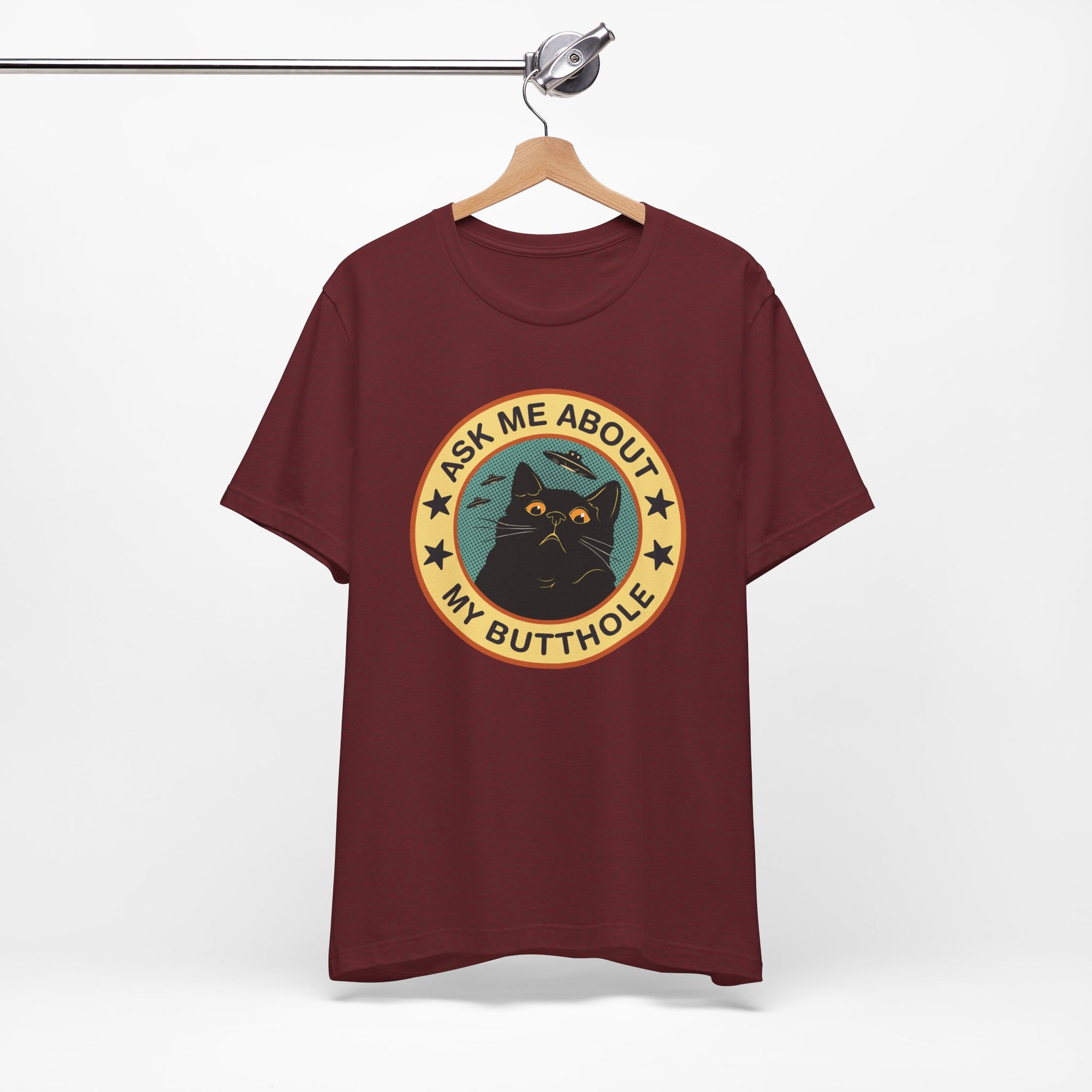 Maroon t-shirt with a graphic design of a cat and text on a hanger against a white background