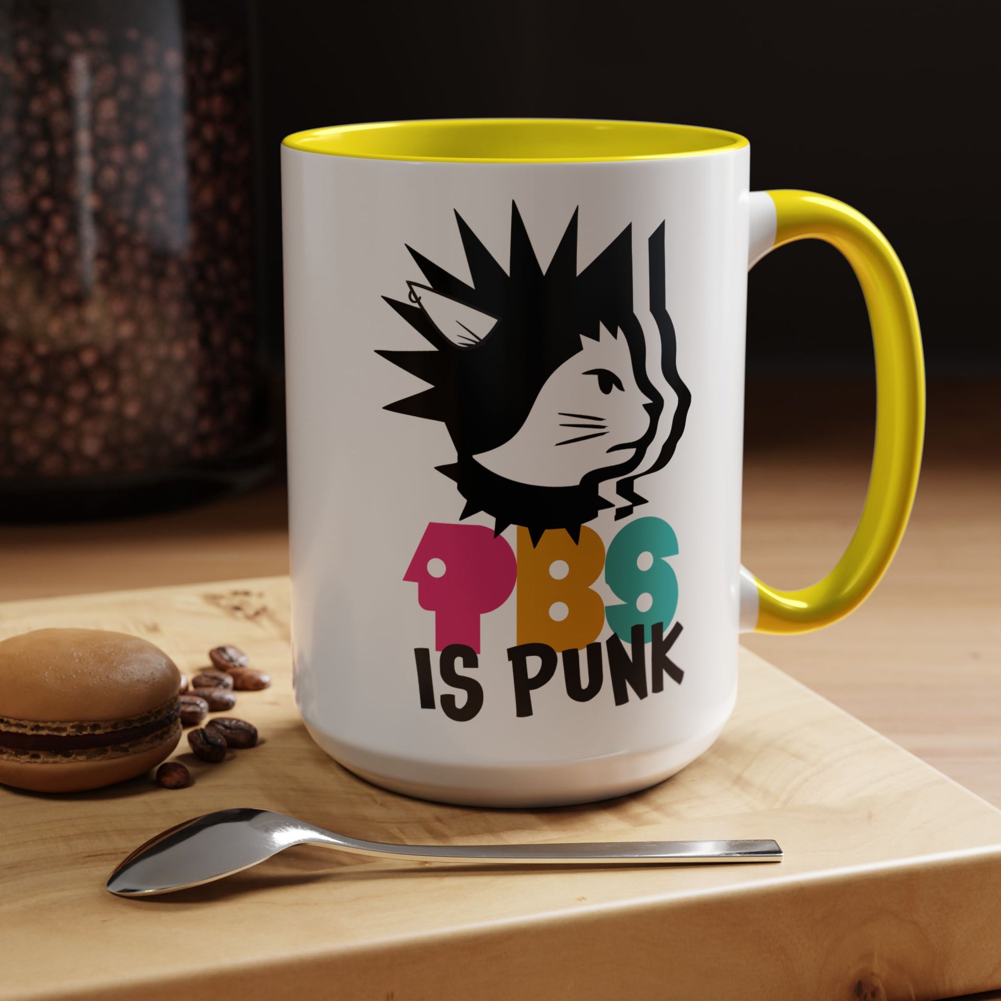Mug with a cat graphic and 'PBS is Punk' text on a wooden surface with coffee beans and a macaron.