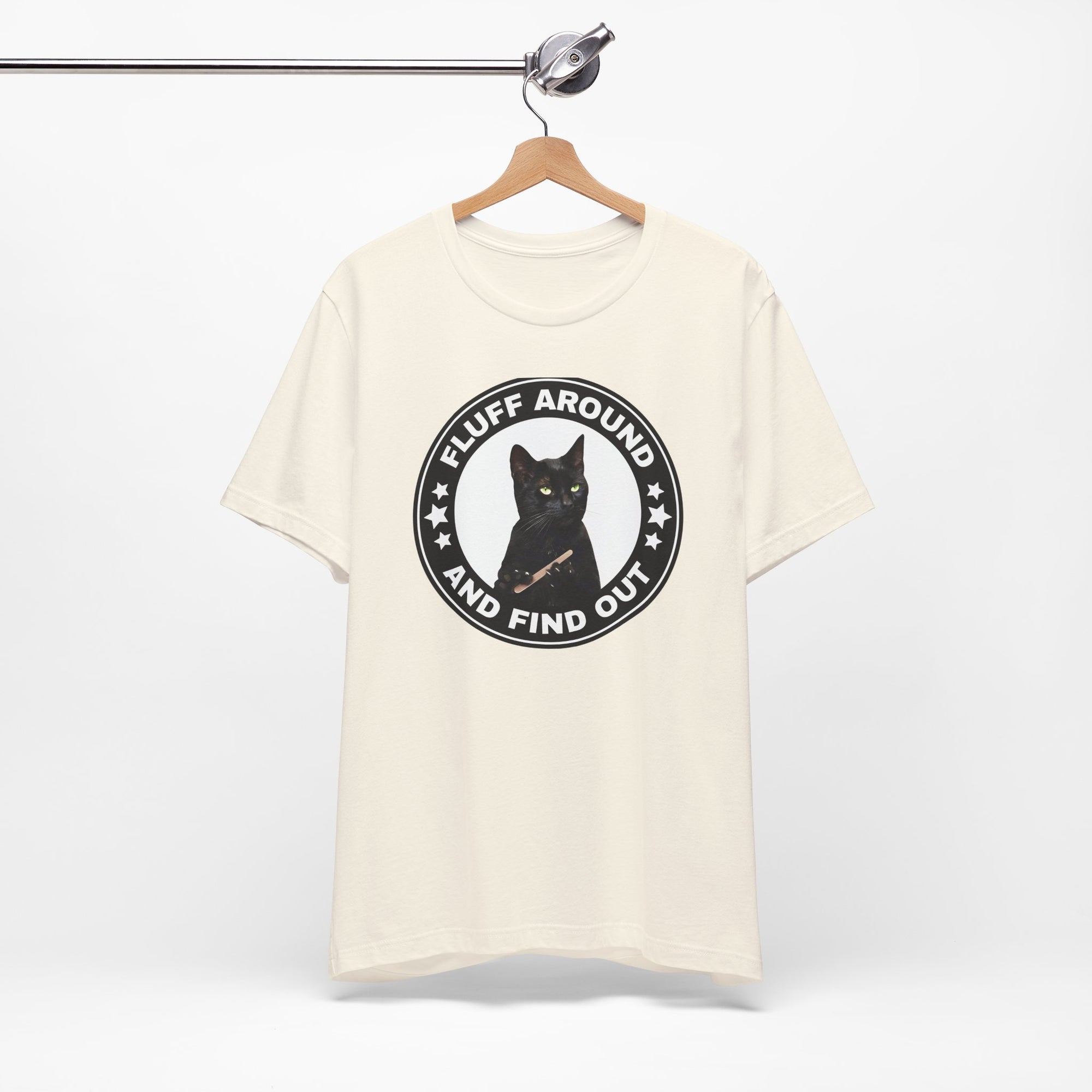 beige t-shirt featuring a circular badge design with a black cat and the phrase “Fluff Around and Find Out.”
