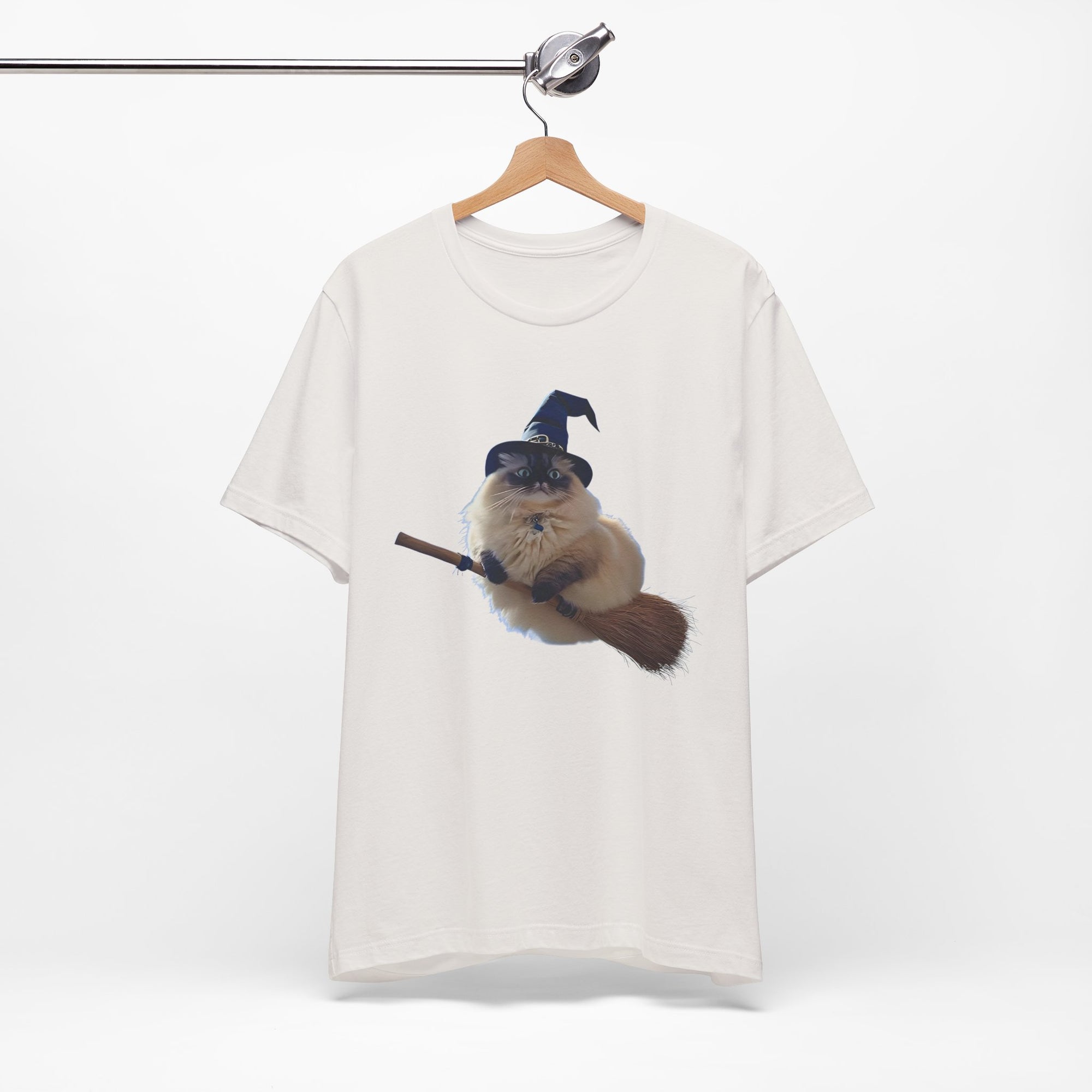White t-shirt with a graphic of a cat wearing a witch hat and holding a broomstick, hanging on a wooden hanger against a white background.