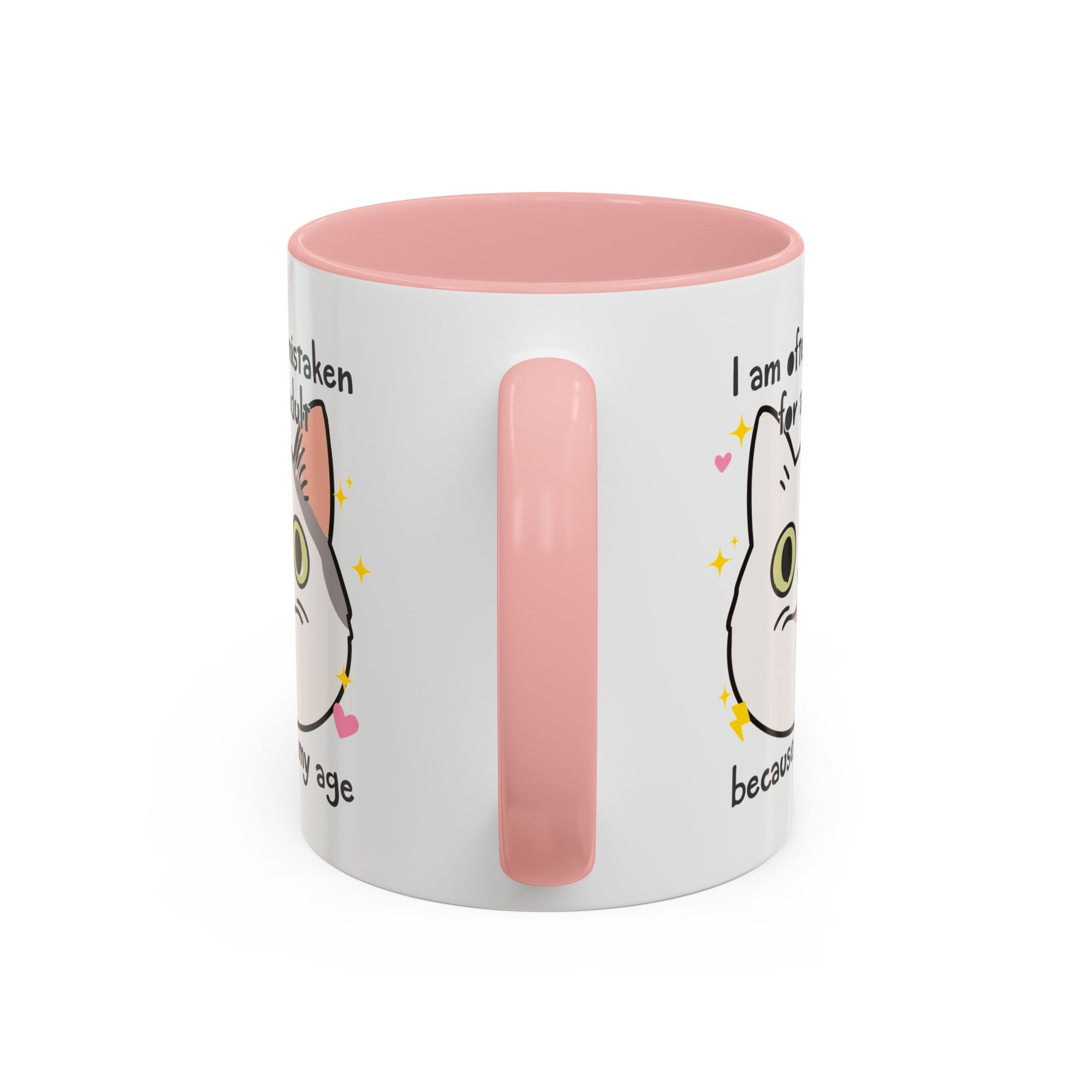 White ceramic mug with peach handle and interior featuring a cute wide-eyed cat face, hearts, sparkles, and the phrase “I am often mistaken for an adult because of my age.”
