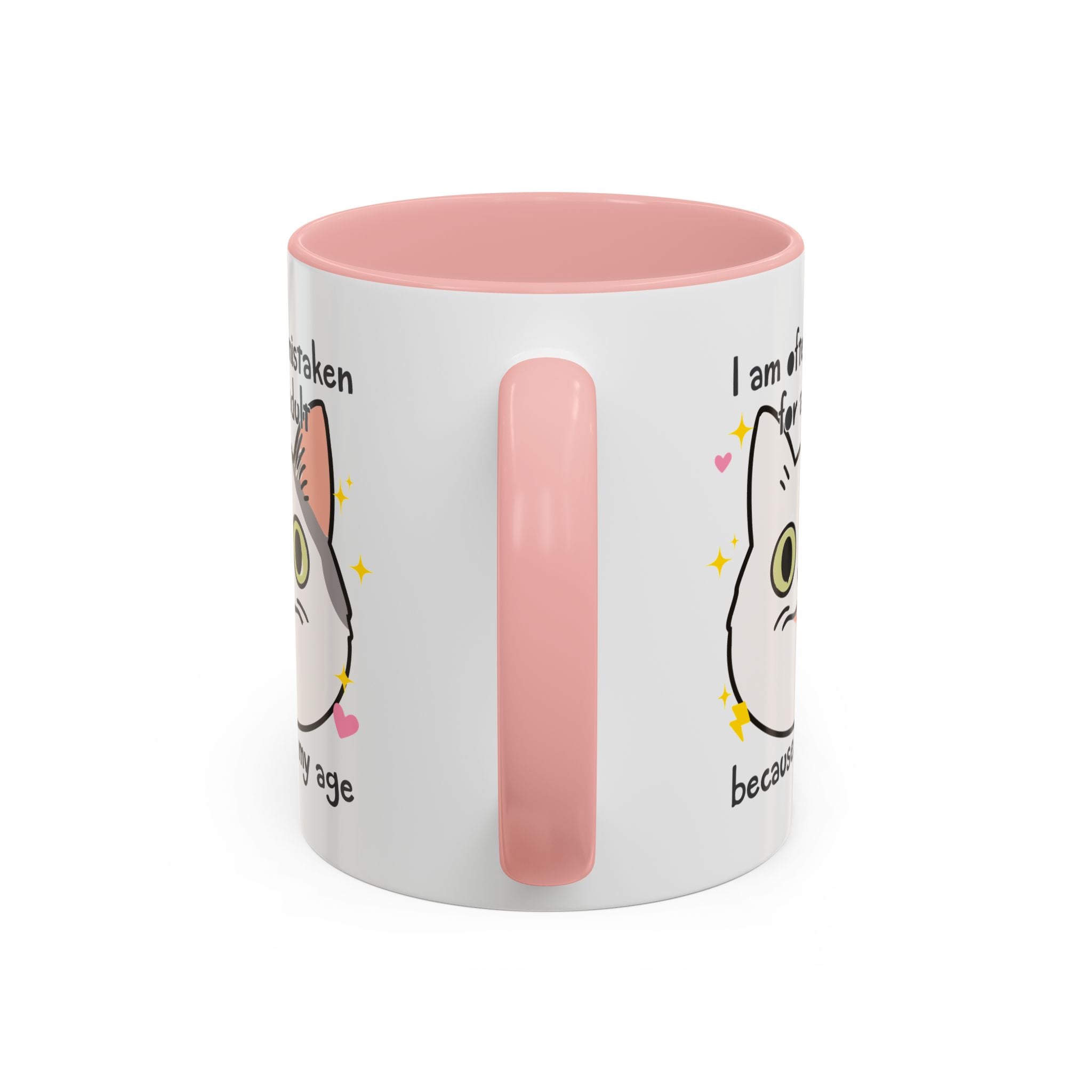 White ceramic mug with peach handle and interior featuring a cute wide-eyed cat face, hearts, sparkles, and the phrase “I am often mistaken for an adult because of my age.”
