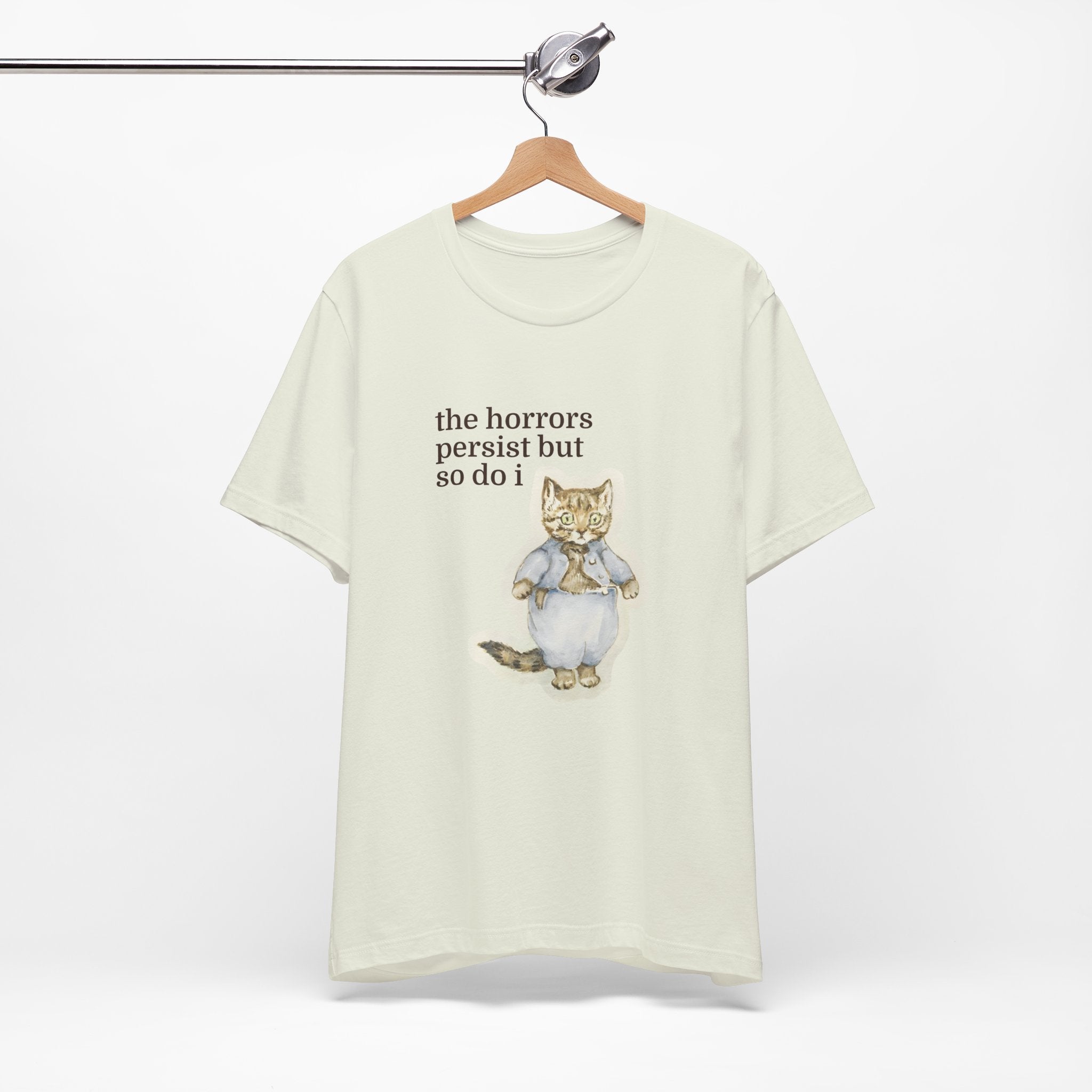 White t-shirt featuring a vintage-style illustrated cat in blue clothing with the phrase “the horrors persist but so do i.”