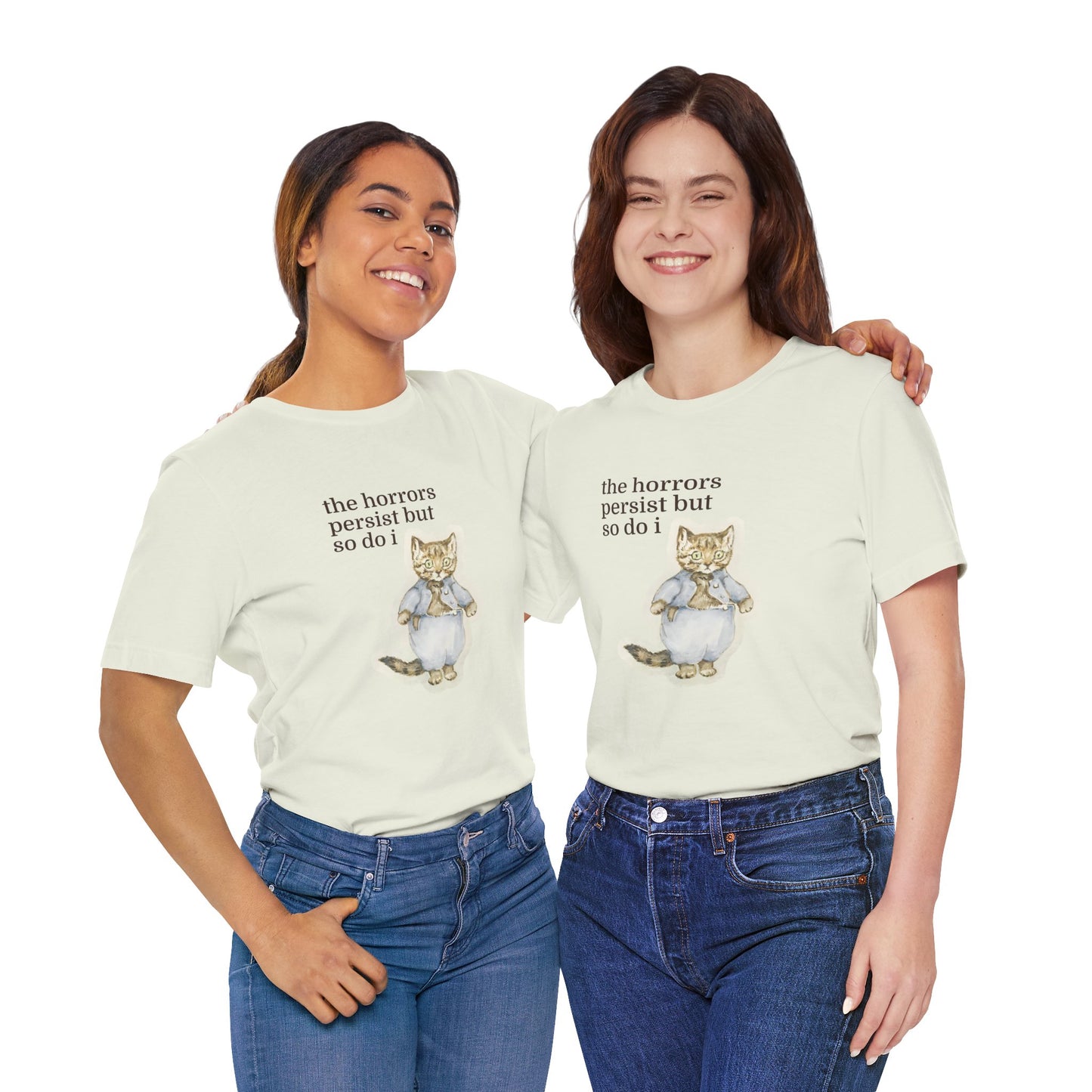 Two women wearing matching beige t-shirt featuring a vintage-style illustrated cat in blue clothing with the phrase “the horrors persist but so do i.”