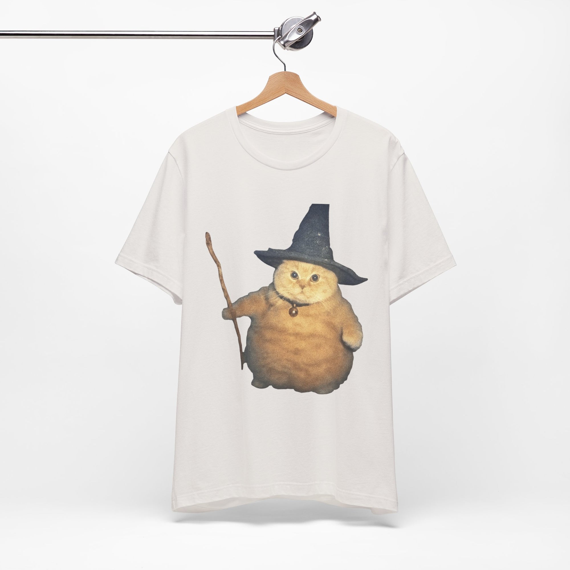 White t-shirt with a graphic of a cat in a witch hat and cape on a hanger against a white background.