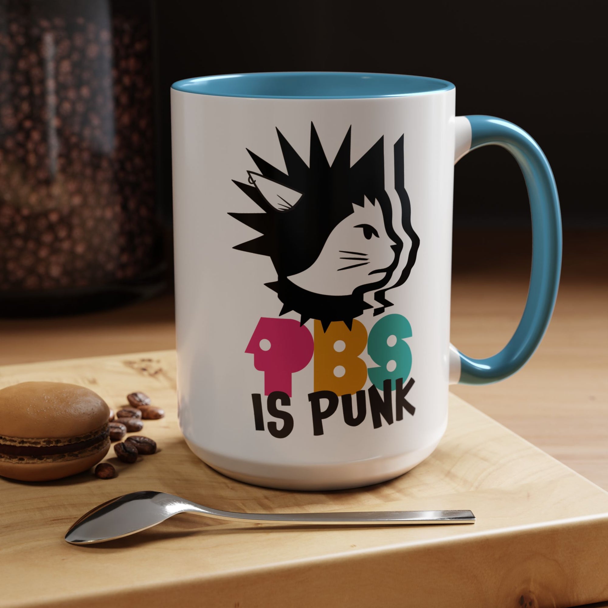 Mug with a cat graphic and 'PBS is Punk' text on a wooden surface with coffee beans and a macaron.