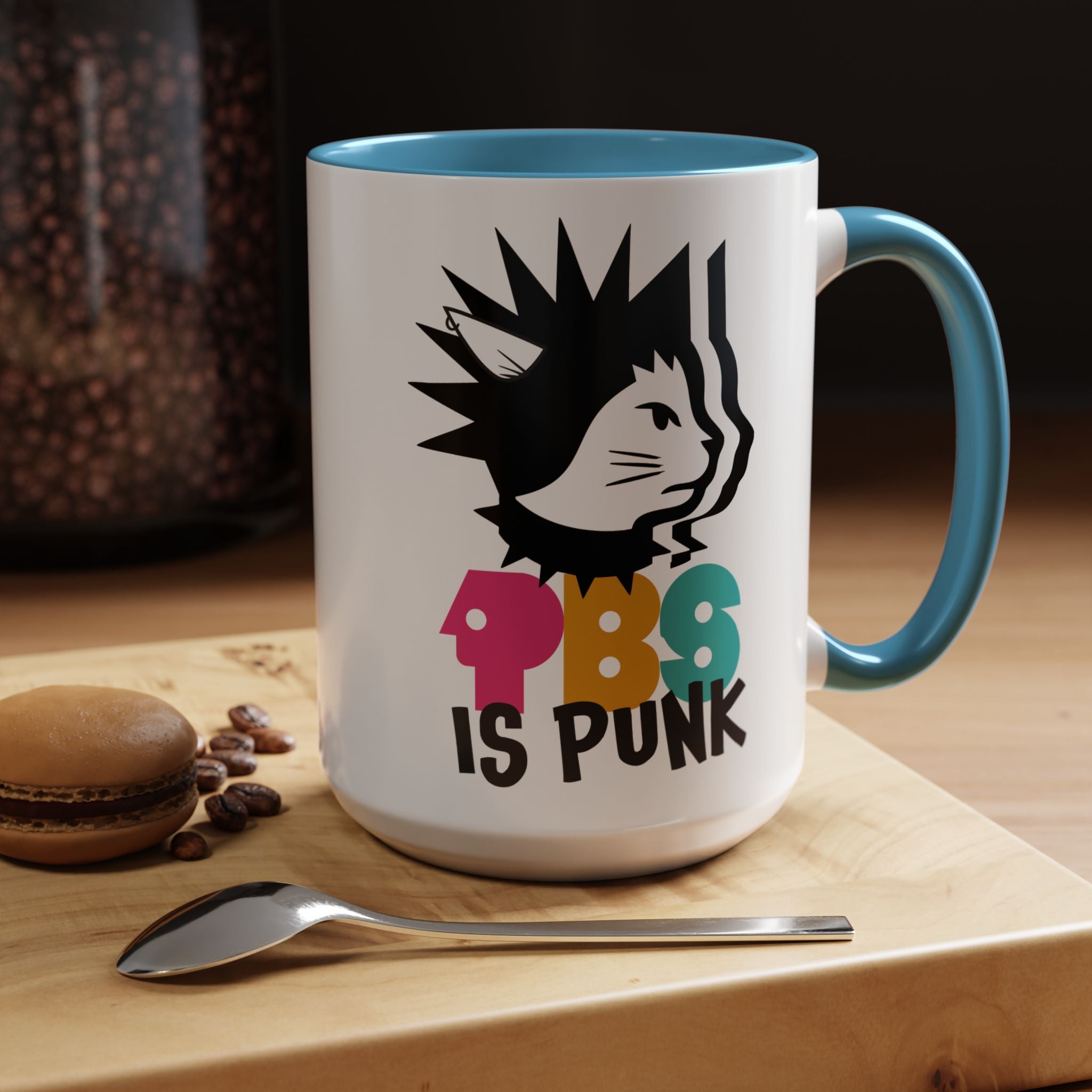 Mug with a cat graphic and 'PBS is Punk' text on a wooden surface with coffee beans and a macaron.