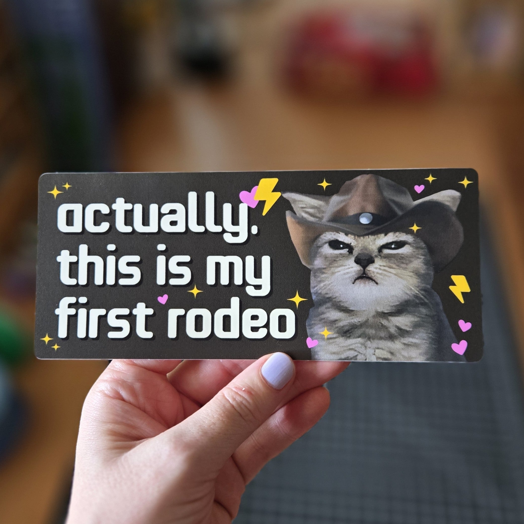 rectangular “Actually, This Is My First Rodeo” bumper stickers with a serious cowboy cat, hearts, sparkles, and lightning bolts.
