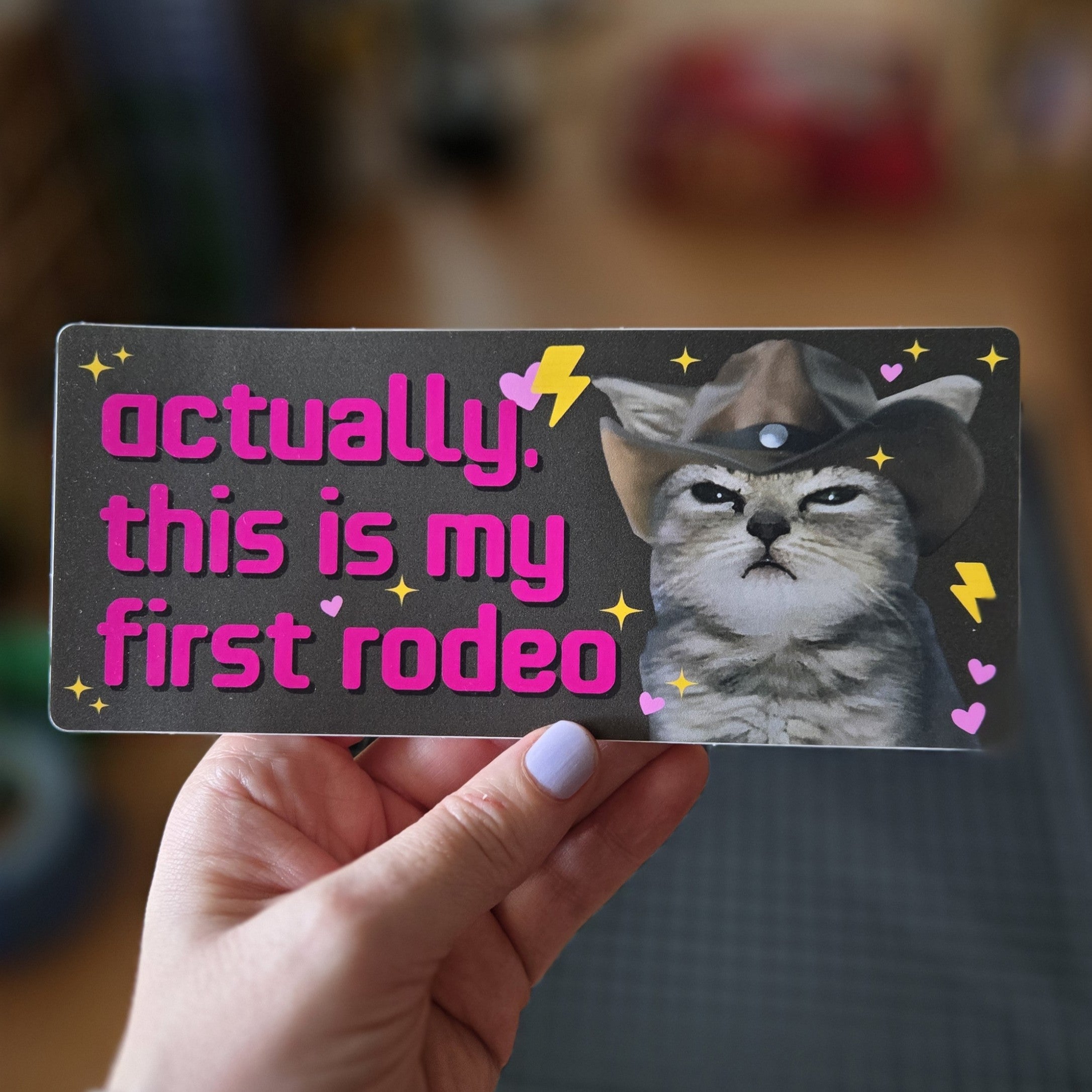 rectangular “Actually, This Is My First Rodeo” bumper stickers with a serious cowboy cat, hearts, sparkles, and lightning bolts.
