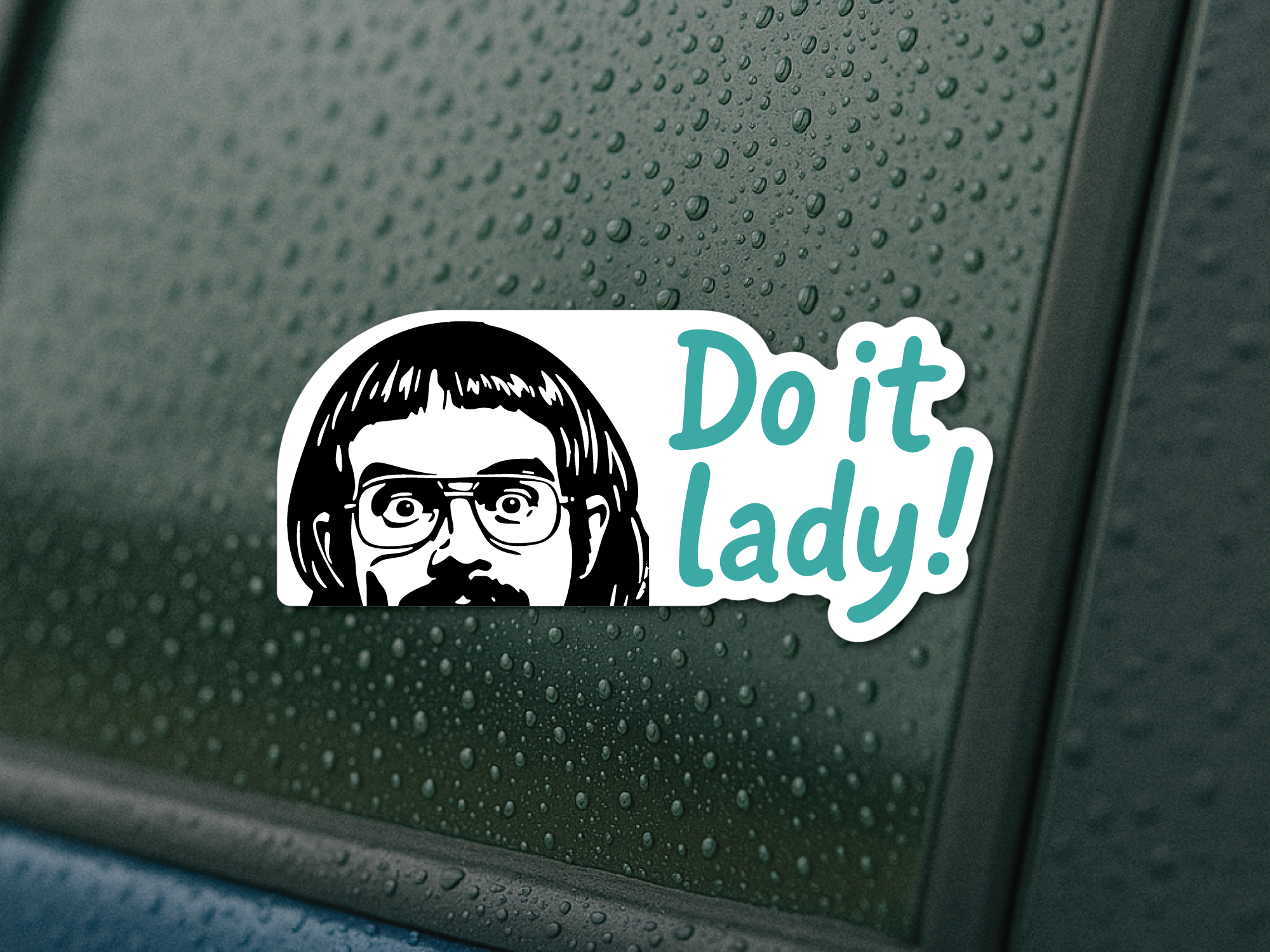 Sticker with a graphic of a person with glasses and text 'Do it lady!' on a wet car window.