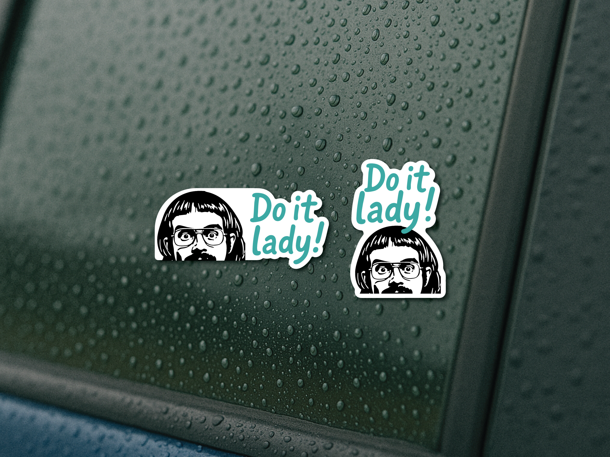 Two “Do It, Lady!” vinyl decals on a rainy car window, shown in opposite orientation options with teal lettering and a black and white peeking character.
