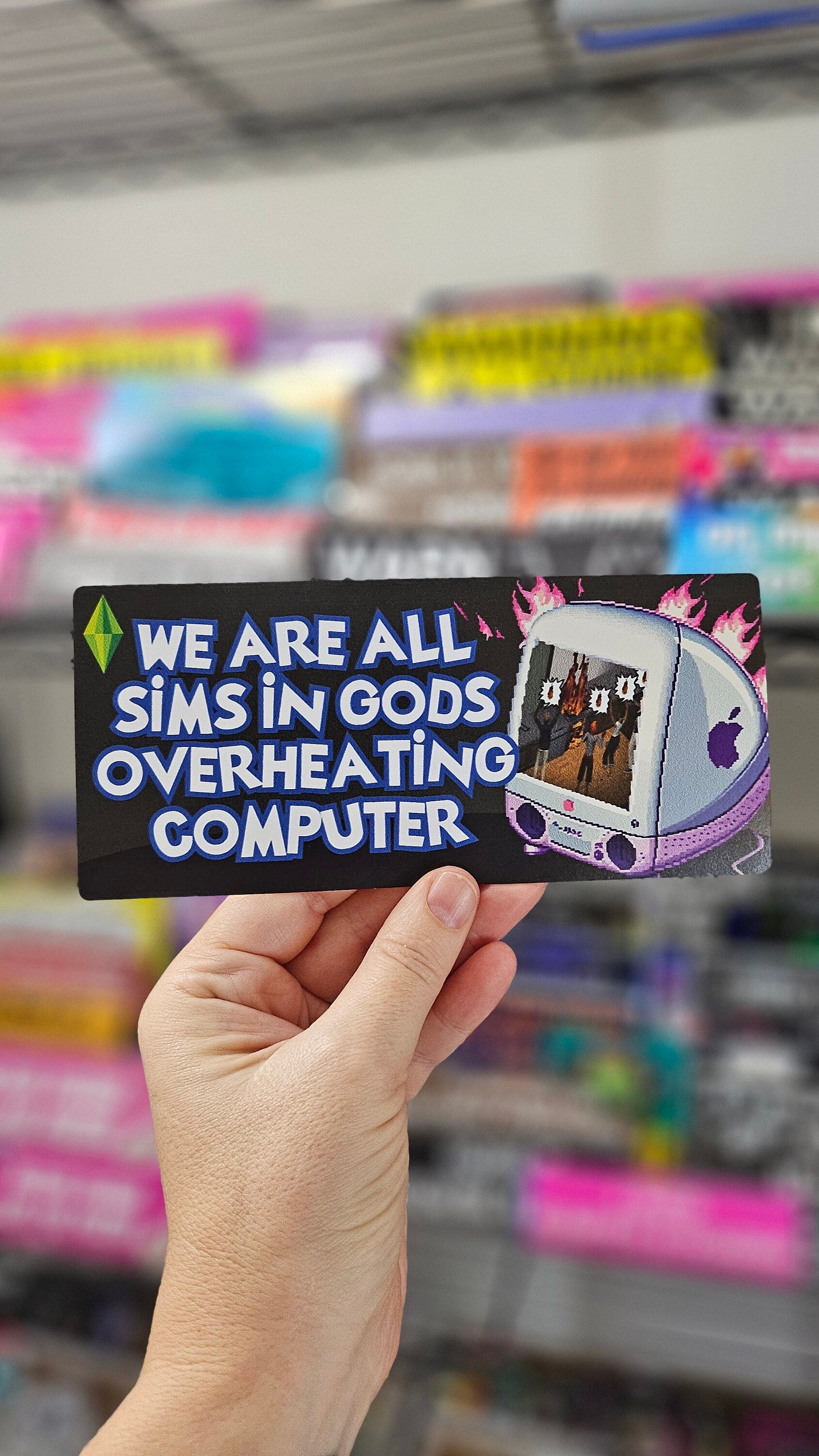  rectangular bumper stickers that say “We Are All Sims in God’s Overheating Computer,” featuring a retro computer, flames, and gamer-style artwork.
