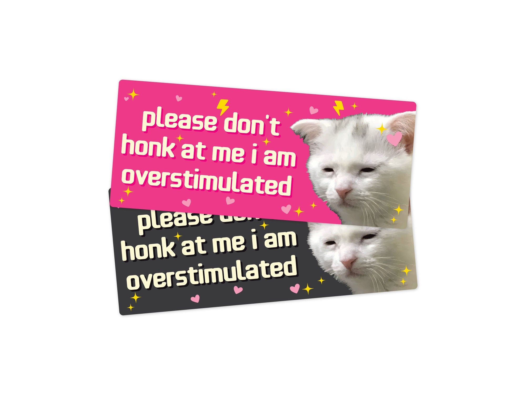 Two rectangular bumper stickers that say “please don’t honk at me i am overstimulated,” shown in pink and dark gray color options with a tired white cat, hearts, sparkles, and lightning bolts.
