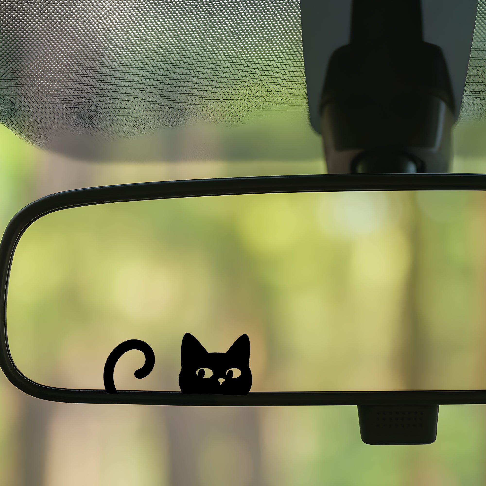 Car rearview mirror with a black cat decal against a blurred green background