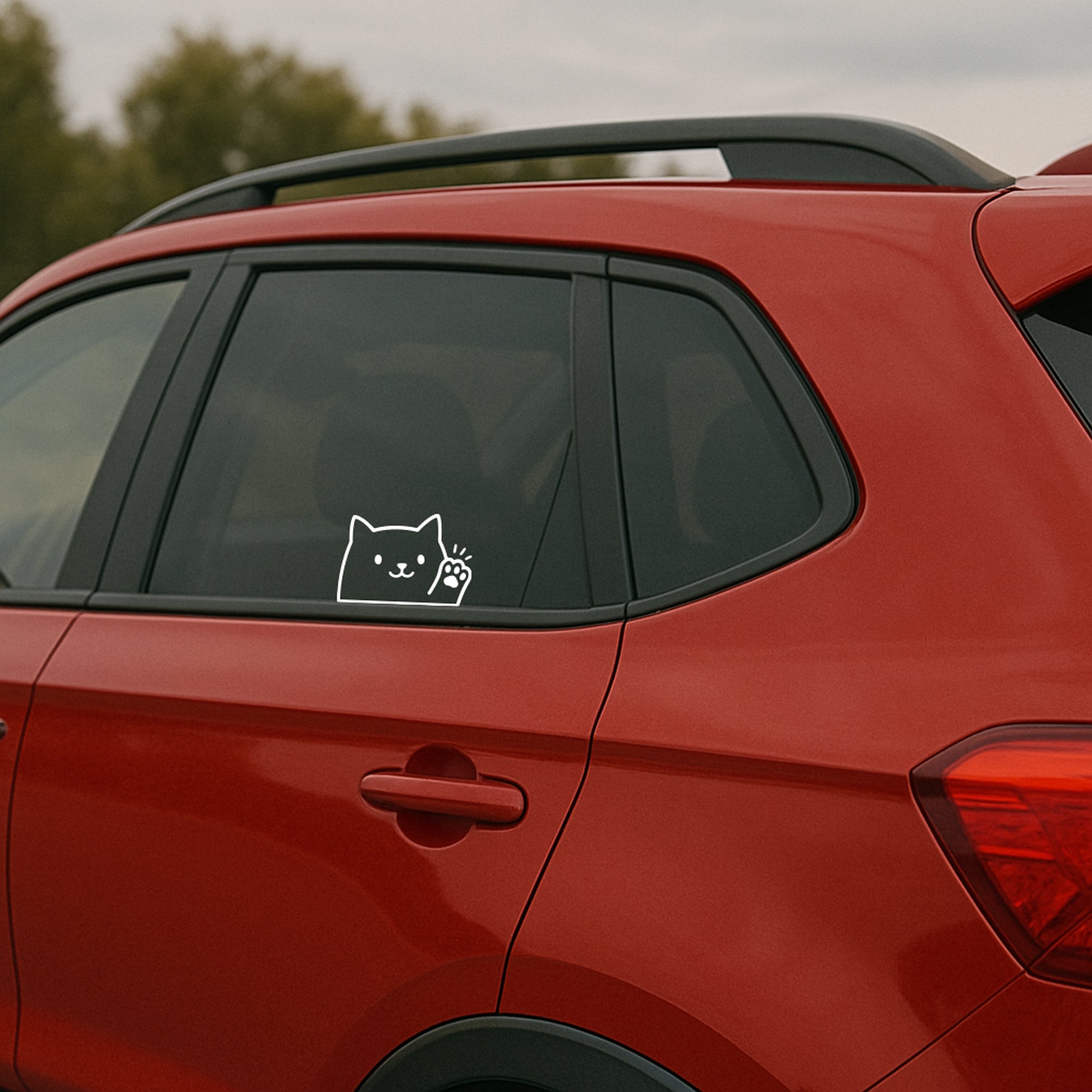 A white transfer decal of a cute cat waving hello or goodbye, applied on a car window with rain droplets.