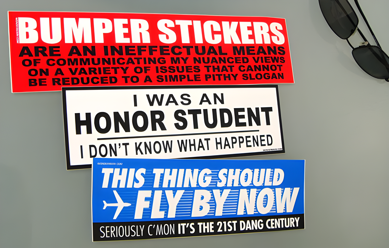 Three bumper stickers on a gray surface with text.