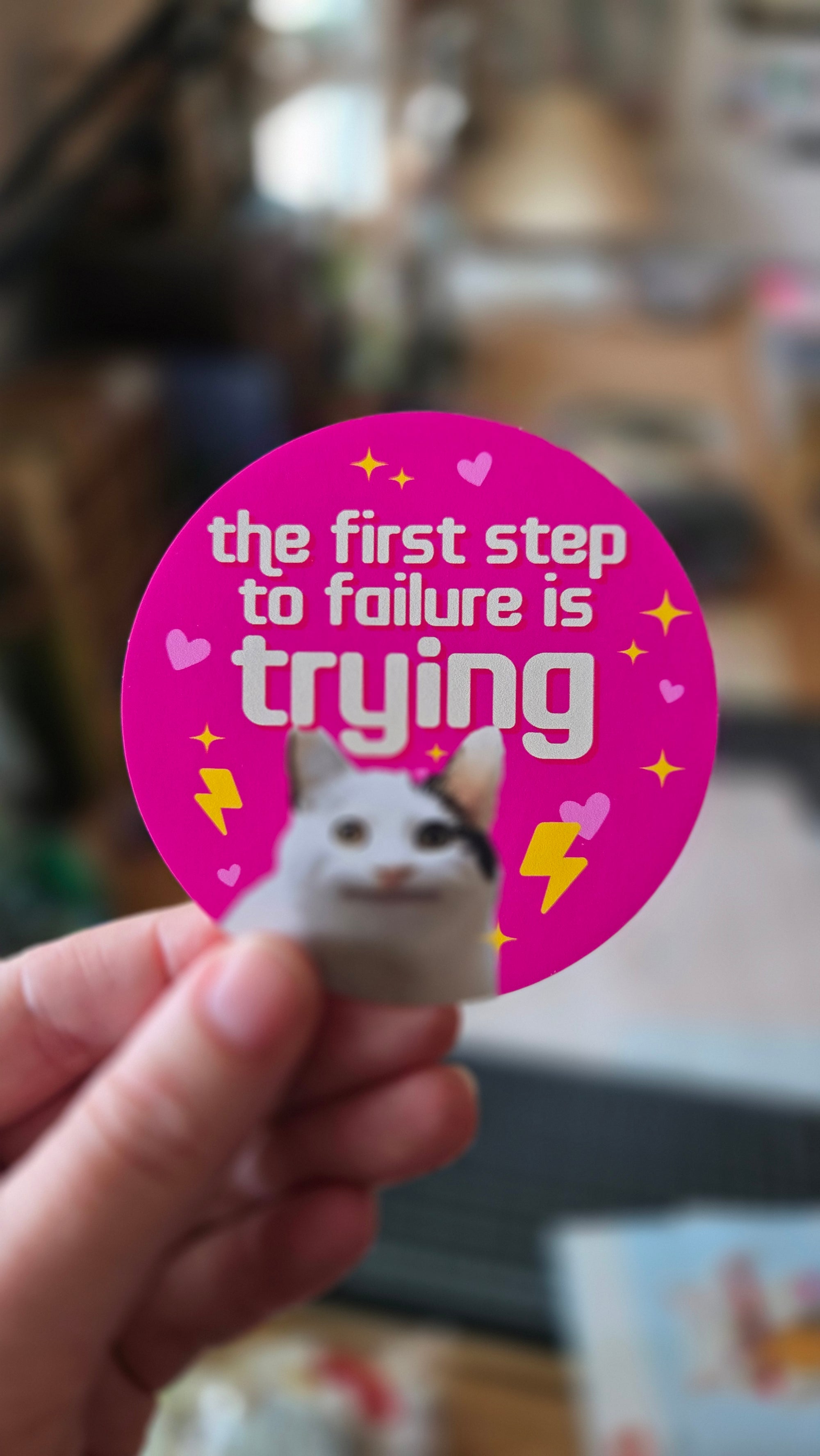 round vinyl sticker options featuring a wide-eyed cat with hearts, sparkles, lightning bolts, and the phrase “the first step to failure is trying.”
