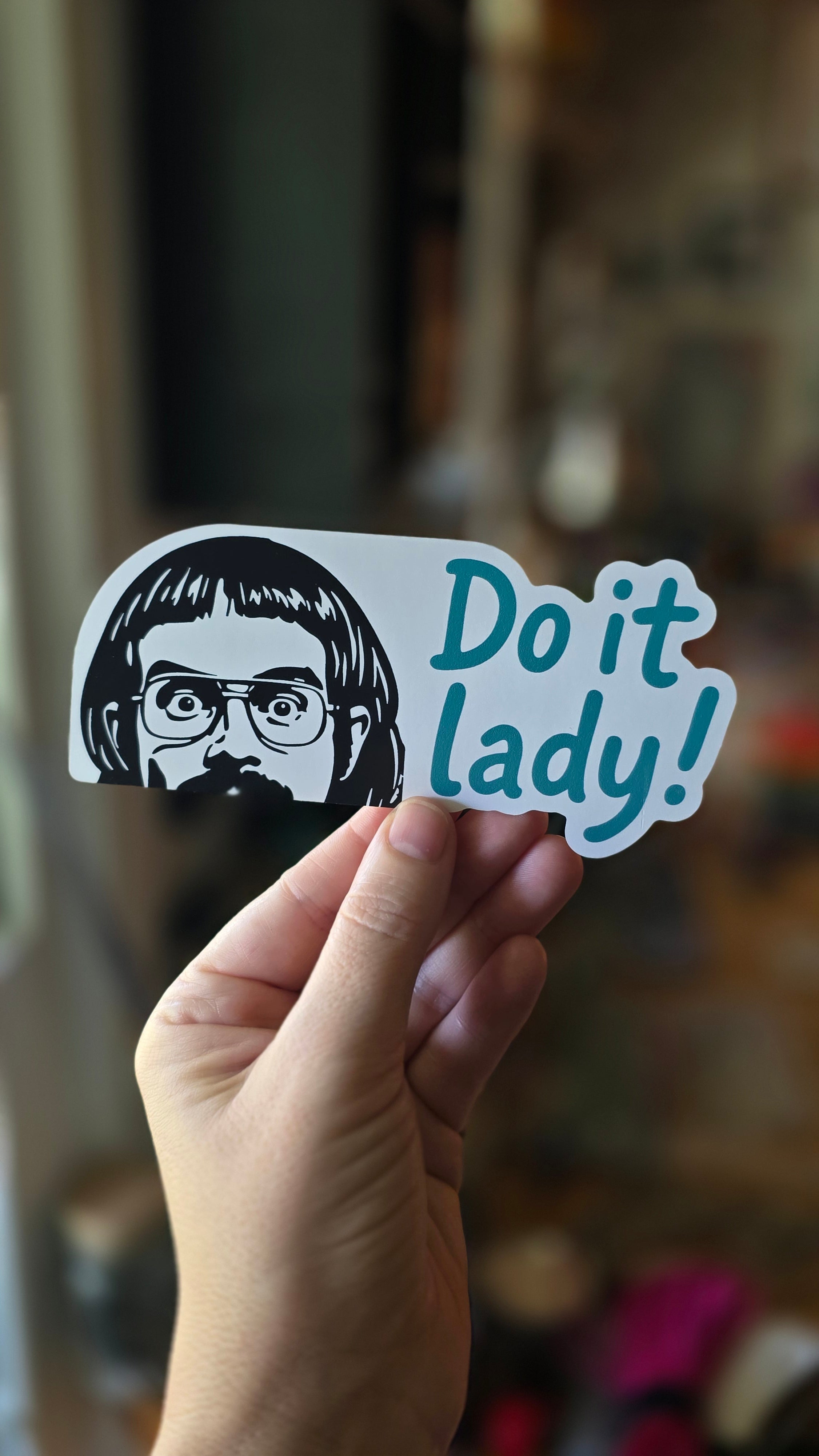 Sticker with 'Do it lady!' text held by a hand against a blurred background
