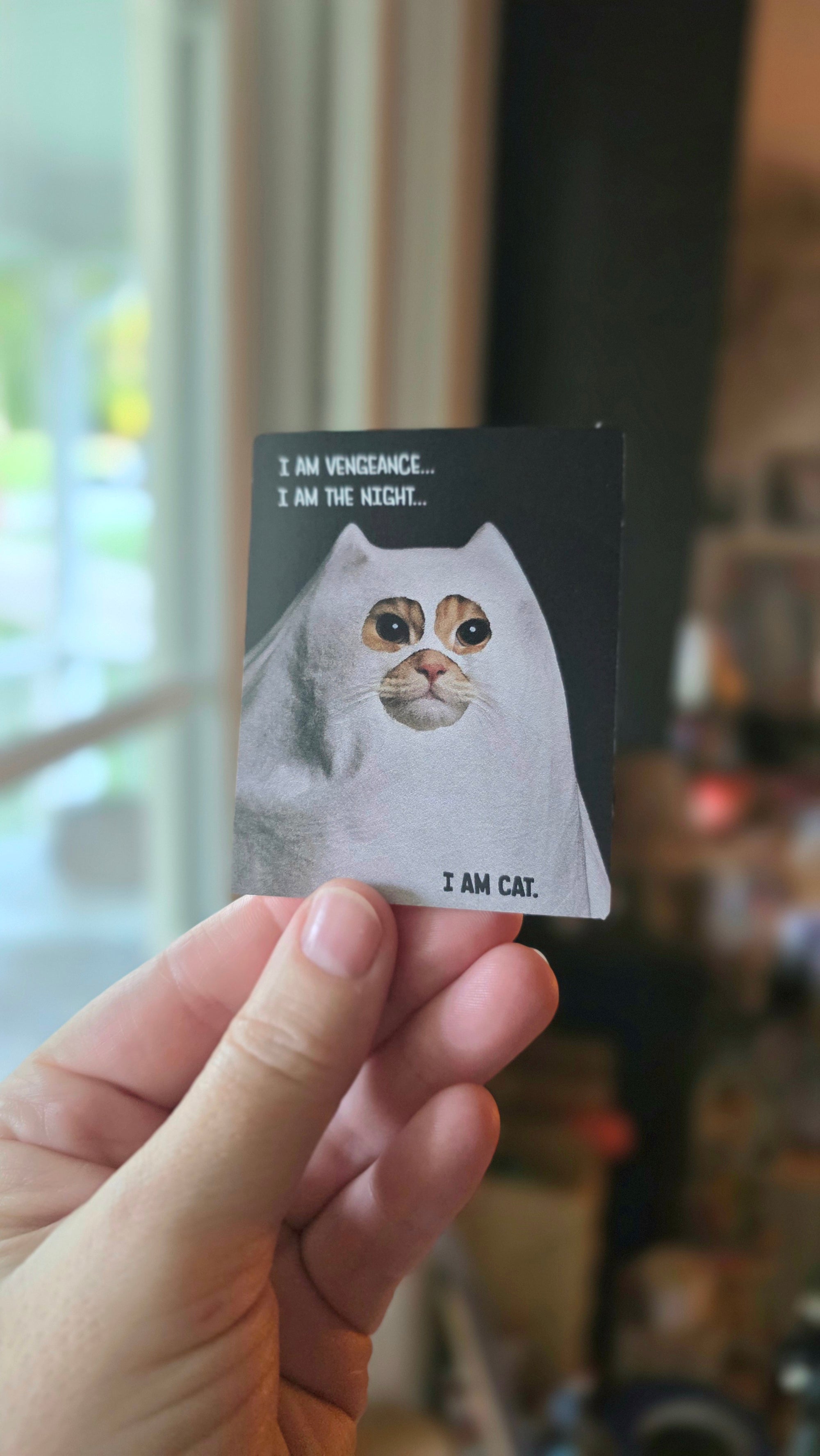 Hand holding a small card with a cat illustration and text.