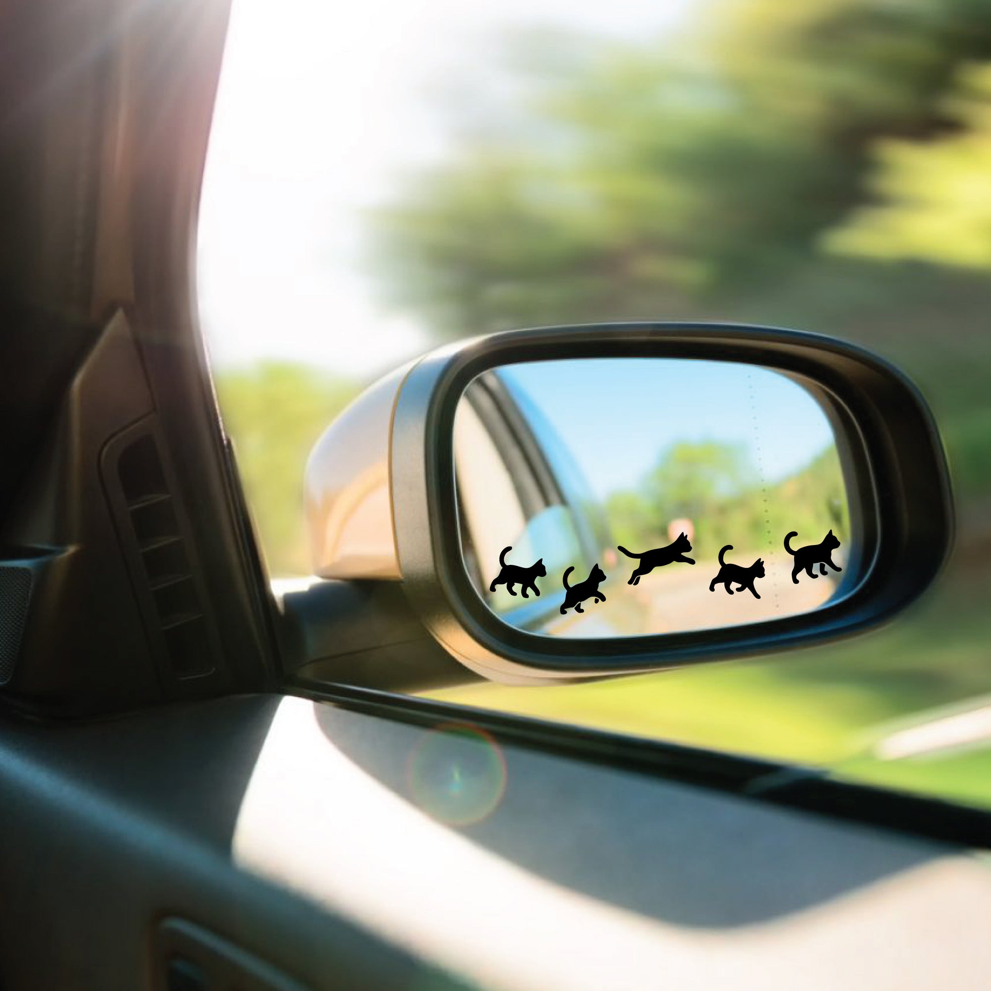 Car side mirror with cat-shaped decals and a blurred green landscape outside